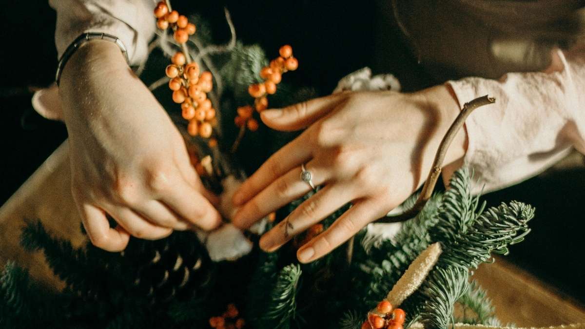 Hands arranging berries and greenery, showing how to work with the best dried flowers for wreath making